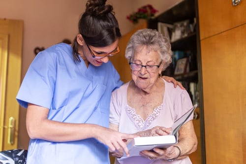 happy-senior-woman-with-her-caregiver-home-reading-book