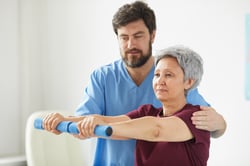 senior-woman-exercising-with-dumbbells-and-male-doctor-helping-her